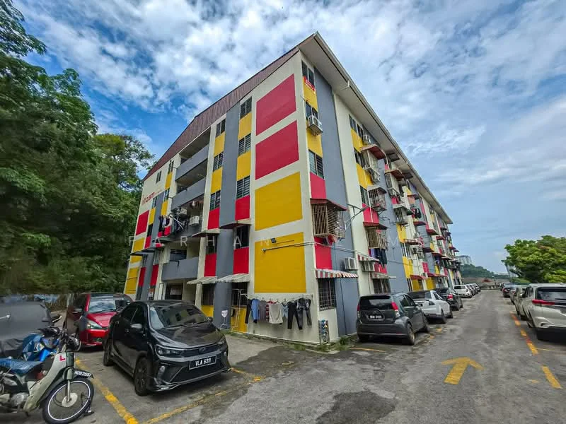 Exterior type: low-rise apartment block; features: yellow painted facade, red painted facade, white painted facade, balconies with railings, visible parking area, multiple parked cars, surrounded by greenery, clothes hanging on balcony; style: modern.
