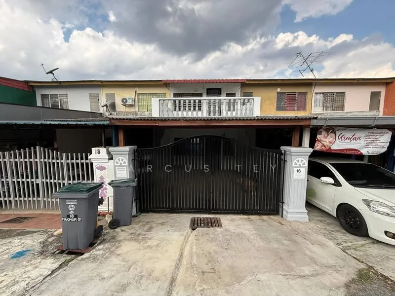 Exterior type: linked terrace house; features: black metal gate, white painted facade, two-storey structure, balcony with railing, visible air conditioning unit, paved driveway, front garden area, multiple parking spaces, signage visible on the building, surrounded by fencing; style: modern.