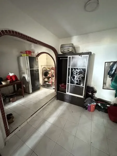 Room features: white tiled flooring, white painted walls, arched doorway, stainless-steel fridge, wooden table, black cabinet with decorative glass, laundry area visible, various household items on the floor.