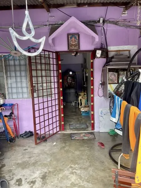 Room features: purple painted walls, concrete flooring, wooden door with grid pattern, decorative wall hanging, ceiling with corrugated metal, open entryway, visible dog, clothes hanging on a line, shoe rack, bicycle, decorative items on the wall; style: traditional.