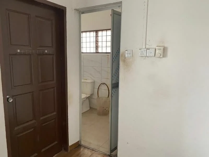 Room features: brown wooden door, mirror on sliding door, white tiled walls, white toilet, light-colored floor tiles, window with grid pattern, light switch, electrical outlets.
