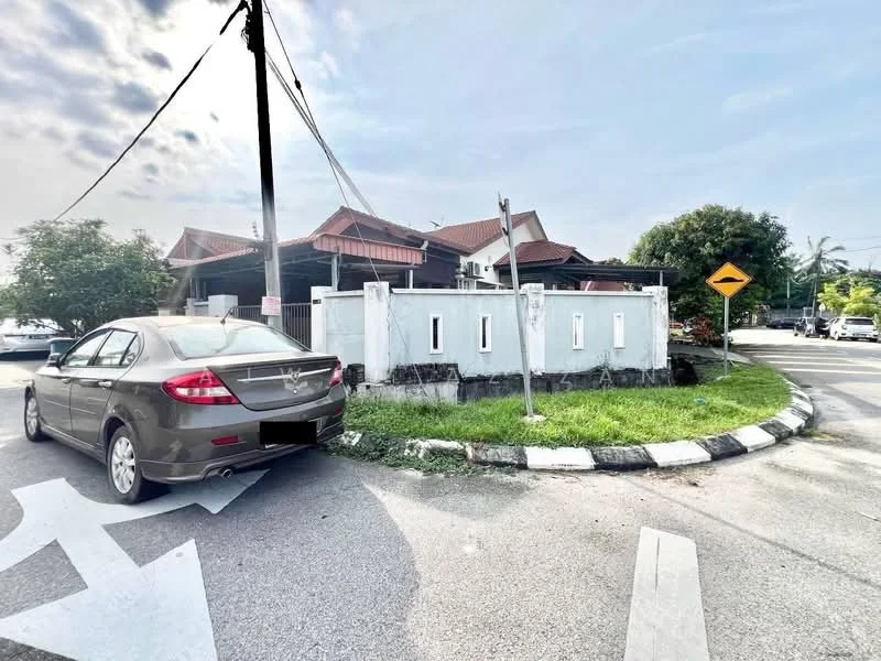 Exterior type: detached bungalow; features: white painted facade, pitched tile roof, surrounded by greenery, manicured lawn, corner lot, driveway, fenced perimeter, street signage, utility poles, road markings; style: traditional.