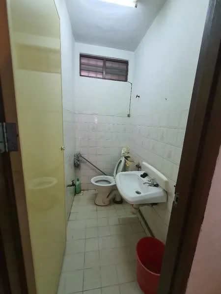 Bathroom features: white tiled walls, white ceramic floor tiles, toilet, sink with faucet, shower area with glass partition, window for natural light, plastic bucket, plumbing fixtures visible.