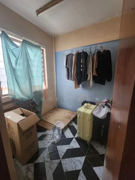 Room features: blue painted wall, cream painted wall, hanging clothes on rack, cardboard box, plastic suitcase, vinyl flooring with black and white pattern, window with sheer curtain, exposed ceiling light fixture.