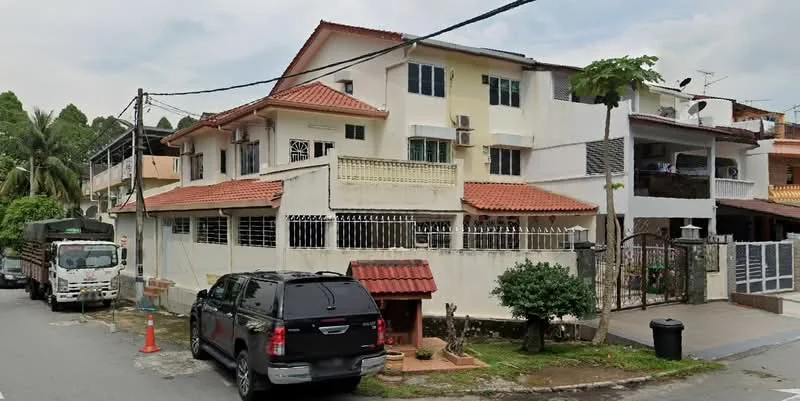 Exterior type: semi-detached house; features: two-storey building, red tiled roof, white painted facade, balconies on upper floor, front garden with small trees, fenced perimeter, driveway with parking space, visible air conditioning units, surrounded by greenery, street view with parked vehicles; style: modern.