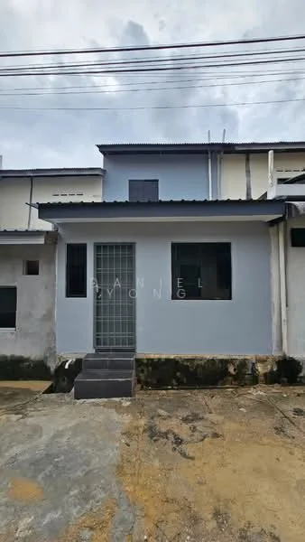 Exterior type: linked terrace house; features: grey painted facade, concrete steps leading to entrance, single front door with security grille, two windows on either side of the door, flat roof, exposed concrete wall, paved driveway, surrounding gravel area; style: modern.