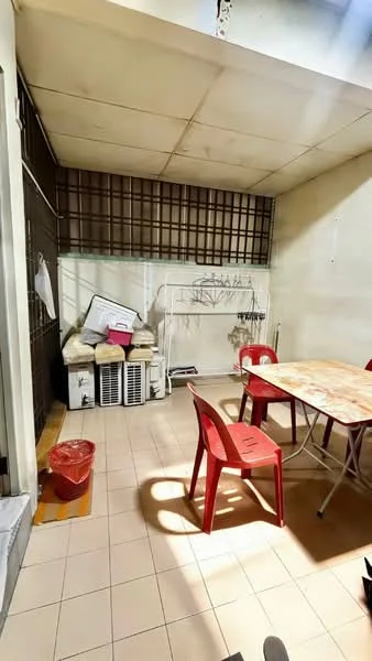 Room features: tile flooring, white painted walls, metal grating on wall, folding table, red plastic chairs, air conditioning units, clothes drying rack, storage boxes, waste bin.