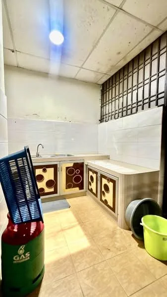 Kitchen features: single-bowl stainless-steel sink, chrome faucet, white tiled walls, brown cabinetry with circular patterns, countertop with stainless-steel finish, gas cylinder, floor tiles in beige, window with metal grille, light fixture on ceiling.