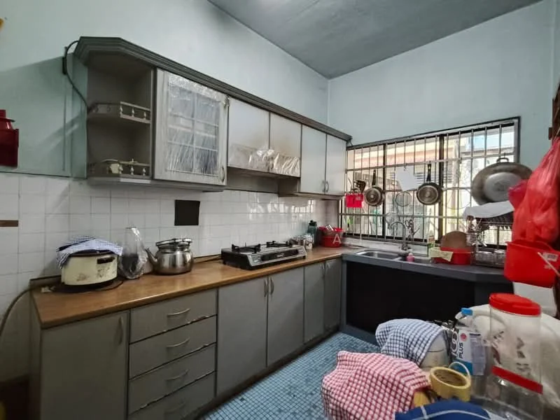 Kitchen features: grey cabinetry, wood countertop, stainless-steel gas stove, stainless-steel sink, chrome faucet, white tiled backsplash, blue mosaic tile flooring, window with security bars, kitchen utensils hanging, rice cooker, plastic containers, dish drying rack.
