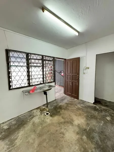 Room features: white painted walls, concrete flooring, metal window grilles, single-basin sink, light fixture on ceiling, wooden door, drainage outlet on floor.