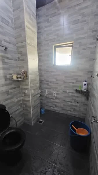 Bathroom features: black toilet, grey tiled walls, grey tiled flooring, window for natural light, shower area, wall-mounted showerhead, shelf for toiletries, bucket, cleaning tools, soap dispenser, toilet paper holder; style: modern.