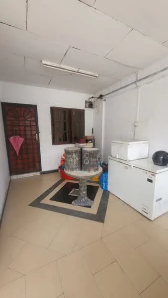 Room features: cream tiled flooring, white walls, ceiling with fluorescent lights, window with brown wooden frame, white chest freezer, decorative stone table, red and blue plastic chairs, black helmet on table, black and white area rug.