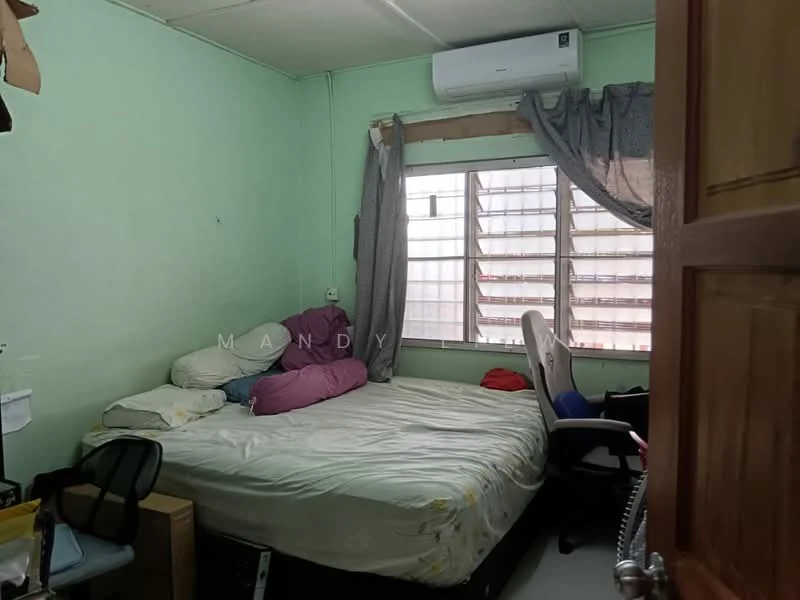 Bedroom features: green painted walls, window with sheer curtains, double bed with white bedding, pillow in various colors, air conditioning unit, office chair, desk chair, wooden door, carpeted flooring.