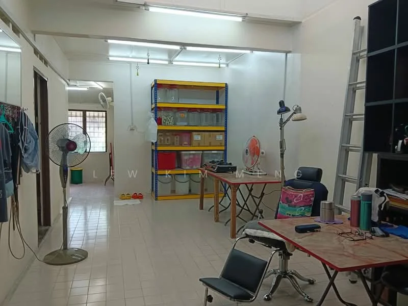 Room features: white painted walls, tile flooring, fluorescent ceiling lights, open shelving unit with colorful storage boxes, folding table, black office chair, standing fan, ladder, clothes hanging on rack; style: minimalist.