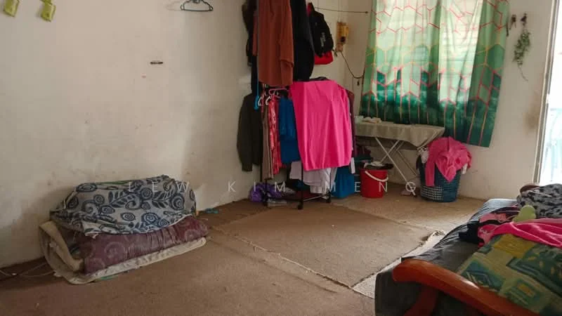 Room features: carpeted flooring, white painted walls, curtains with geometric pattern, clothes hanging on wall hooks, folding table, baskets for storage, two beds with bedding, various clothing items on display; style: minimalist.