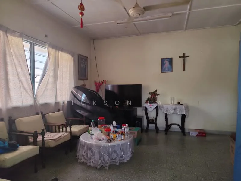 Living features: cream painted walls, ceiling fan, window with sheer curtains, wooden sofa set with cushions, round table with lace tablecloth, television on stand, decorative wall art, cross on wall, flooring with green tiles; style: traditional.