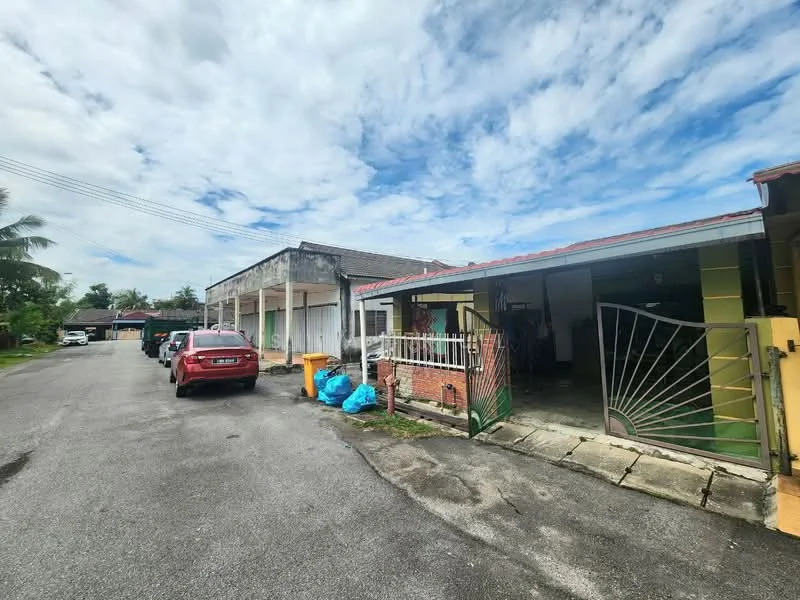 Exterior type: semi-detached house; features: single-storey, red tiled roof, exposed brick facade, green painted walls, front gate with decorative metalwork, driveway with interlocking pavers, manicured lawn, surrounded by palm trees, street view with parked cars, clear blue sky; style: traditional.