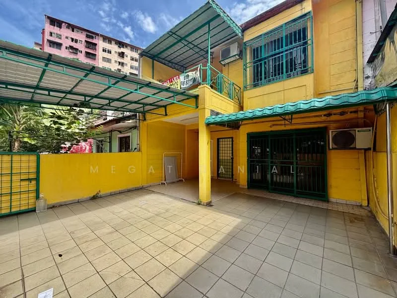 Exterior type: semi-detached house; features: yellow painted facade, flat roof with green awning, tiled flooring, exposed brick wall, air conditioning unit visible, manicured landscaping, fenced outdoor area, balcony with railing, multiple storeys, surrounded by greenery; style: traditional.