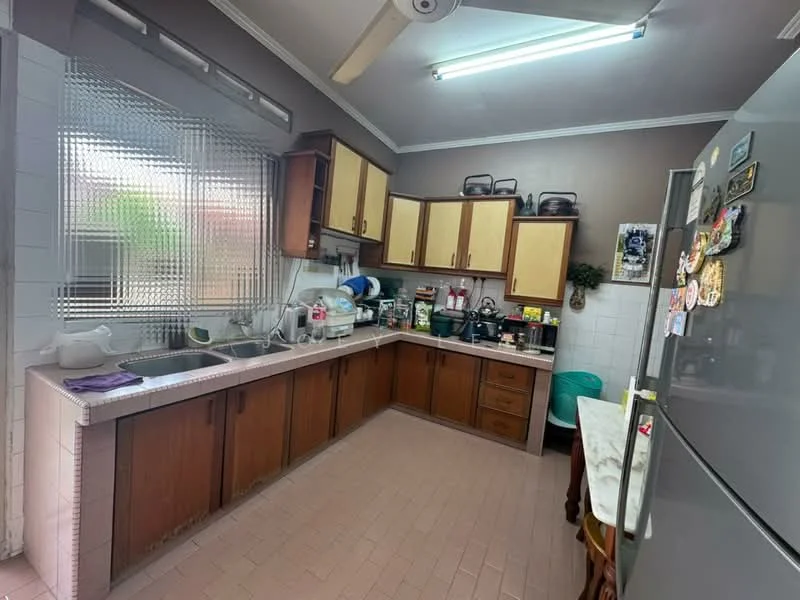 Kitchen features: L-shaped countertop, brown wooden cabinetry, double-bowl stainless-steel sink, chrome faucet, white tiled backsplash, built-in refrigerator, kitchen appliances including kettle and blender, ceiling fan, window with frosted glass, light fixture, tile flooring, green plastic chair; style: traditional.