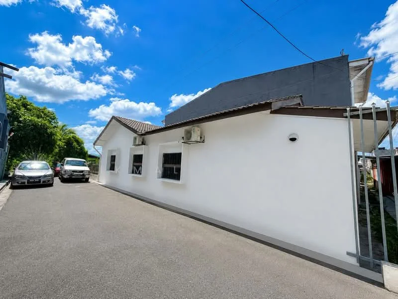 Exterior type: detached bungalow; features: white painted facade, flat roof, 2 wall-mounted split AC units, driveway with asphalt surface, manicured landscaping, windows with security bars, parking space for multiple vehicles; style: modern.