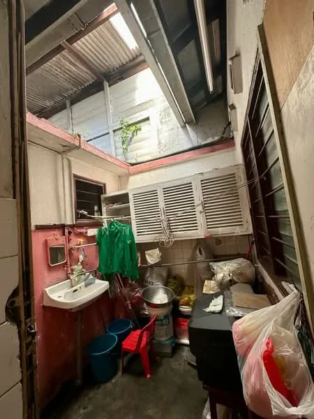 Room features: sink with wall-mounted faucet, red painted walls, metal roof, exposed beams, wooden cabinets, plastic storage bins, black table, red plastic chair, various kitchen utensils, natural light from skylight, green plants, concrete flooring; style: functional.