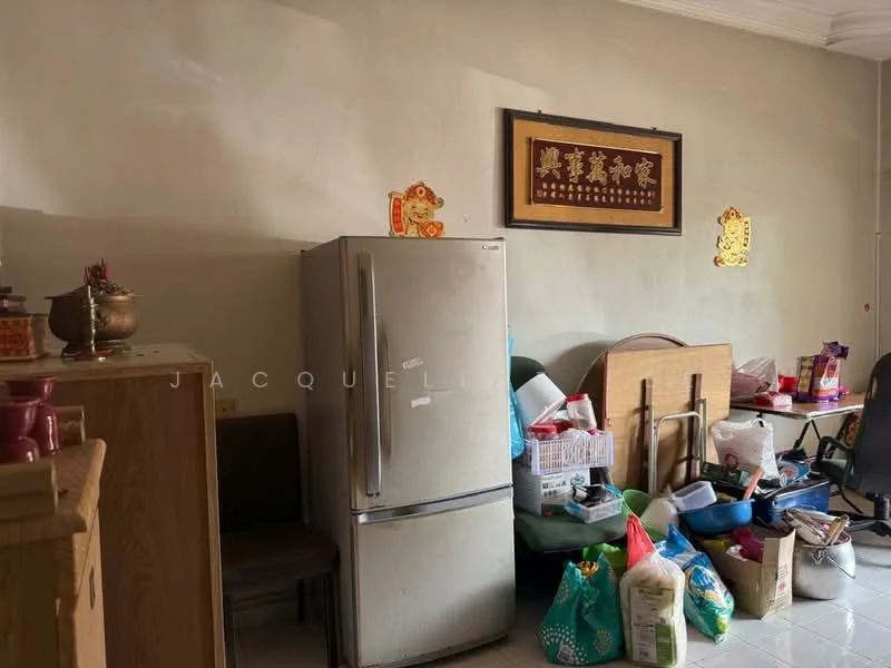Room features: light beige painted walls, white tiled flooring, stainless-steel fridge, wooden cabinet, multiple plastic storage bags, two wooden tables, various decorative items, wall-mounted artwork, cluttered space.