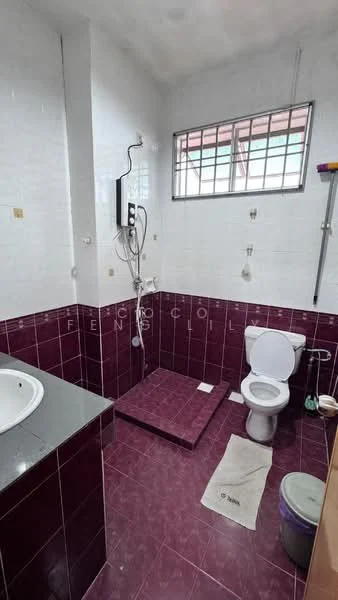 Bathroom features: white toilet, shower area with glass partition, chrome shower head, wall-mounted shower mixer, white sink with grey countertop, tile flooring in maroon, white tiled walls, window for natural light, bath mat on floor, purple waste bin.