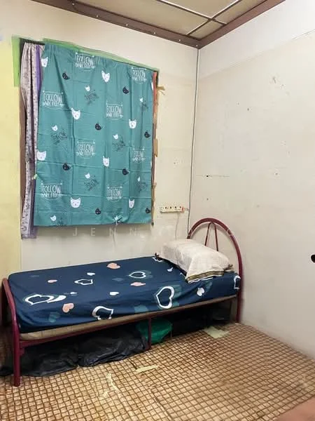 Bedroom features: single bed with metal frame, mattress with patterned bedding, pillow on bed, green curtain with cat pattern, bare walls, tiled flooring, small bedside area, wall-mounted electrical outlets.