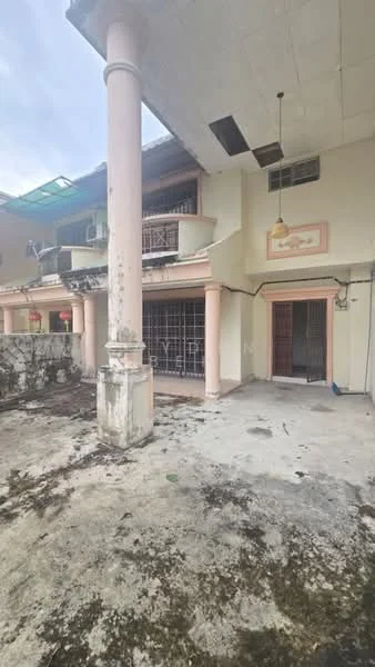 Exterior type: semi-detached house; features: two-storey structure, pink painted columns, balcony on upper floor, exposed concrete flooring, overgrown landscaping, metal grilles on windows, partially covered roof, visible drainage, outdoor space with debris, faded exterior paint; style: traditional.