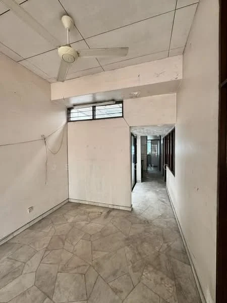 Room features: plain white walls, ceiling with tiles, 5-blade ceiling fan, flooring with patterned tiles, window with grille, doorway leading to hallway, natural light from windows, unpainted surfaces, no visible furniture; style: minimalist.