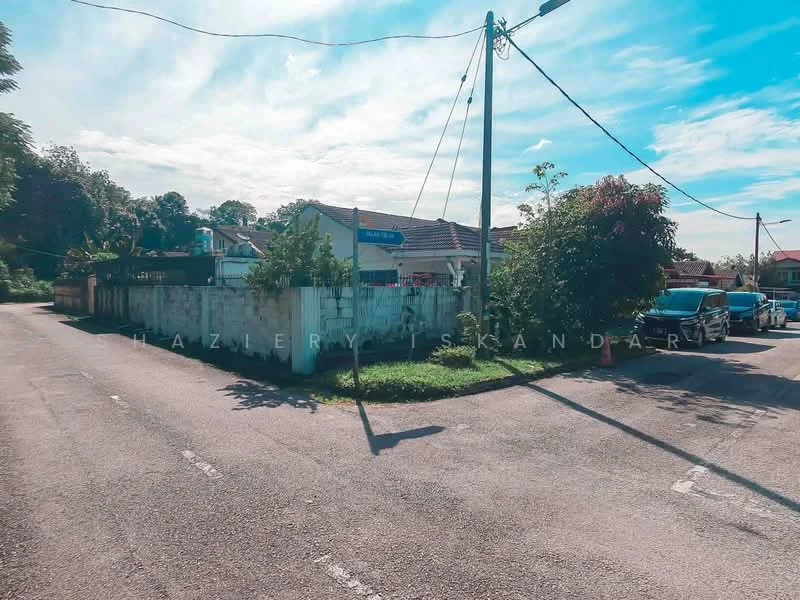 Exterior features: single-storey building, surrounded by greenery, residential street, paved road, utility poles, street signage, fenced property, driveway with parked car.