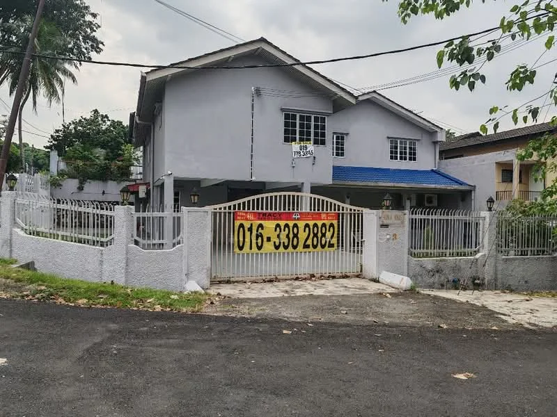 Exterior type: detached bungalow; features: grey painted facade, flat roof with blue tiles, white wrought iron gate, fenced perimeter, manicured lawn, paved driveway, outdoor lighting fixtures, surrounded by trees, single-storey, front porch, visible signage for sale; style: modern.
