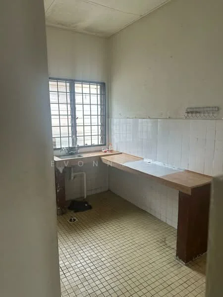 Room features: white tiled walls, brown wooden countertops, single window with metal grille, yellow tiled flooring, sink area, open space layout, no visible appliances, minimal decor.