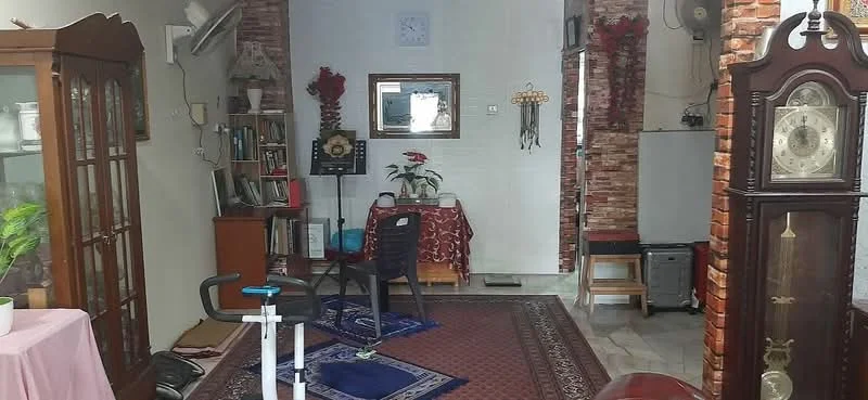 Living features: exposed brick walls, white painted walls, marble tile flooring, area rug with geometric pattern, wooden display cabinet, wall-mounted clock, decorative plants, traditional grandfather clock, small table with tablecloth, black plastic chair, bookshelf, artwork on wall, air conditioning unit; style: traditional.