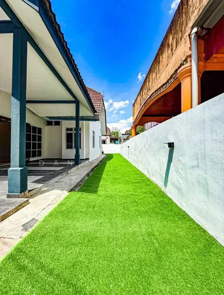 Exterior type: detached bungalow; features: artificial grass lawn, paved walkway, side yard, white painted walls, roof overhang, clear blue sky, adjacent building with orange accents; style: modern.