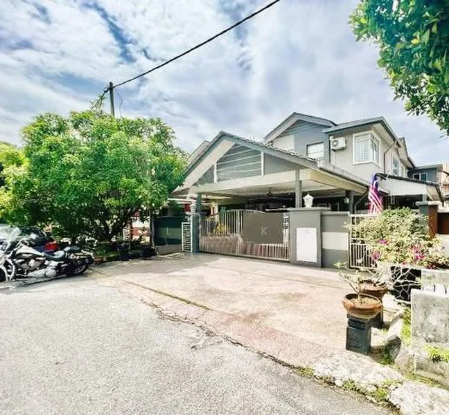 Exterior type: semi-detached house; features: grey painted facade, pitched tile roof, manicured lawn, mature trees, paved driveway, fenced front yard, car porch with awning, visible motorcycles parked, flagpole with flag, outdoor plants in pots; style: modern.
