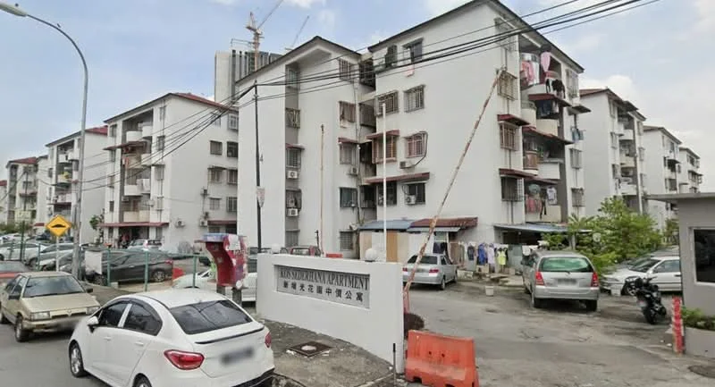 Exterior type: low-rise apartment block; features: white painted facade, red tiled roof, multiple balconies, visible air conditioning units, parking lot, signage at entrance, surrounded by greenery, street view, construction in background; style: modern.