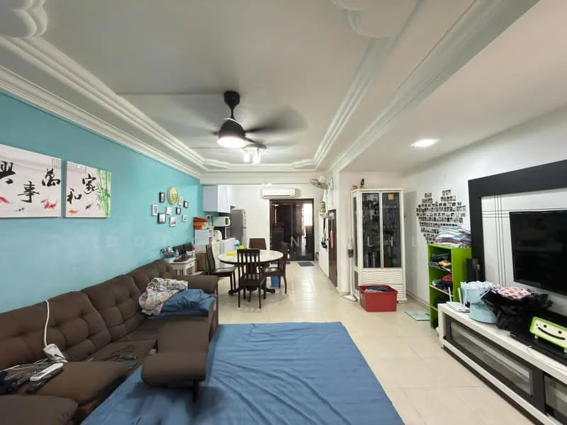 Living features: brown fabric sectional sofa, blue area rug, ceiling fan with light, wall-mounted TV, white entertainment unit, decorative wall art, light-colored tiled flooring, crown moulding on ceiling, open layout to kitchen, green shelving unit, dining area visible in background; style: modern. Kitchen features: white cabinetry, stainless-steel appliances, open layout to living area, light-colored tiled flooring; style: modern.