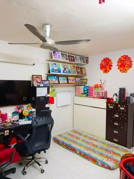 Room features: white painted walls, tile flooring, 5-blade ceiling fan, wall-mounted TV, black desk with computer, red office chair, shelves with framed photos, storage cabinet, colorful mattress on the floor, decorative wall art, multi-colored storage bins; style: modern.