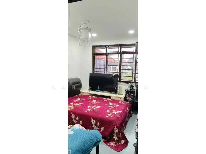 Living features: red floral patterned bedspread, black leather sofa, wooden TV console, flat-screen TV, white painted walls, recessed LED downlights, large window with grid pattern, light blue throw blanket, grey flooring; style: modern.
