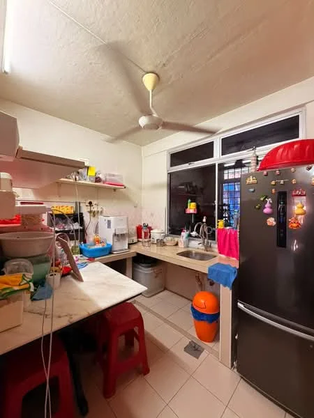 Kitchen features: white painted walls, tile flooring, ceiling fan, marble countertop, stainless-steel fridge, kitchen cabinets, sink with faucet, microwave, kettle, colorful plastic containers, red plastic stools, window with view.