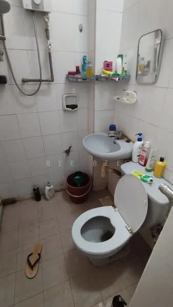 Bathroom features: white tiled walls, cream tiled flooring, shower with handheld showerhead, wall-mounted mirror, toilet, single-sink vanity, soap dispenser, various toiletries on shelves, waste bin, potted plant, slippers on the floor.