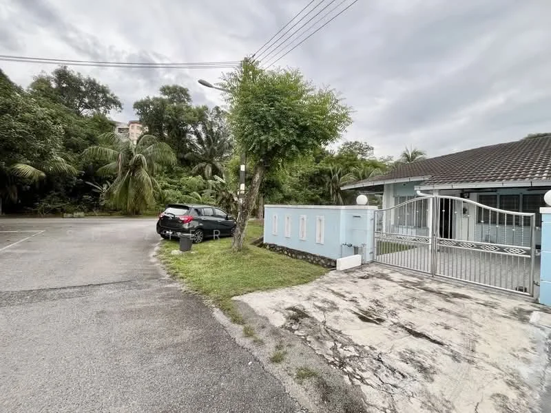 Exterior type: detached bungalow; features: single-storey building, grey tiled roof, light blue painted facade, manicured lawn, paved driveway, gate with decorative metalwork, surrounded by tropical landscaping, parking space for 1 car, street view, adjacent to greenery; style: modern.