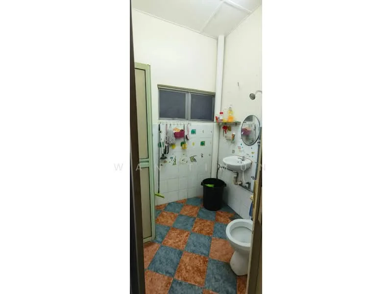 Bathroom features: white tiled walls, blue and orange checkered floor tiles, one-piece toilet, round mirror, sink with faucet, shower head, window for natural light, towel rack, various hooks for towels, cleaning supplies on wall hooks.