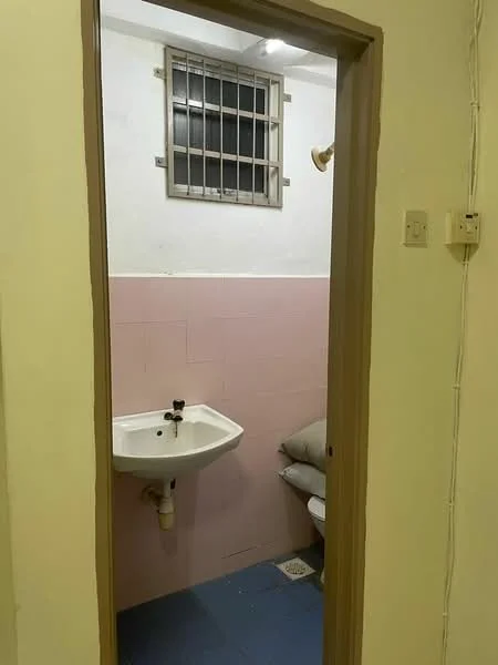 Bathroom features: white wall tiles, pink accent wall, blue tile flooring, wall-mounted sink, chrome faucet, toilet, window with security bars, shower head, light fixture.