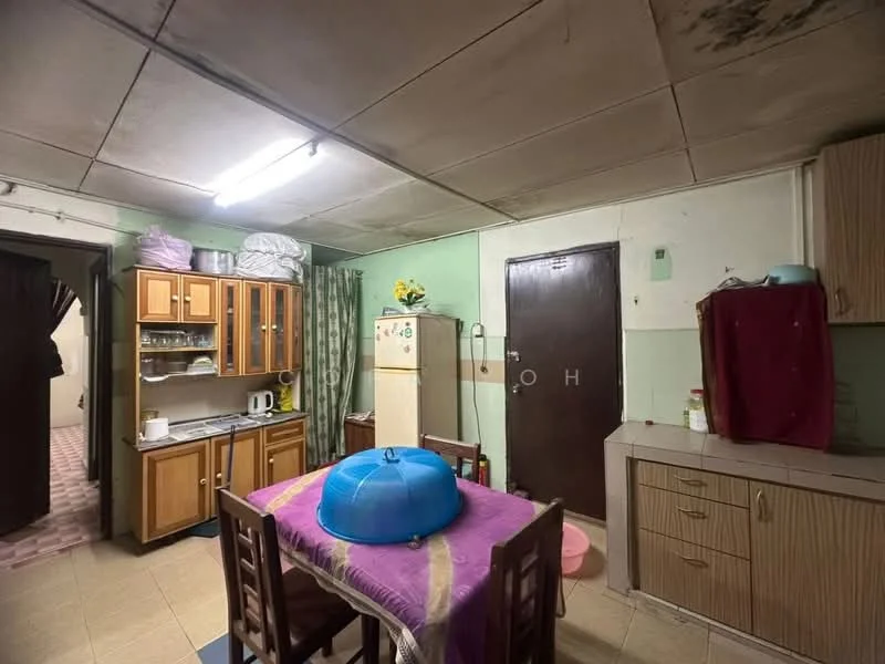 Kitchen features: brown wooden cabinetry, white countertop, stainless-steel fridge, white ceramic sink, chrome faucet, dining table with four wooden chairs, green walls, tile flooring, fluorescent ceiling light, curtains on window, open shelving, wall-mounted cabinet.