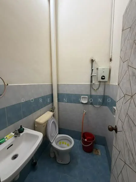 Bathroom features: white toilet, white sink, blue tiled walls, grey tiled flooring, shower with glass enclosure, water heater, toilet paper holder, bucket, faucet, drain, wall-mounted mirror.