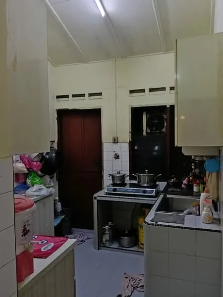 Kitchen features: white painted walls, tile flooring, single-bowl stainless-steel sink, chrome pull-down faucet, 4-burner gas hob, built-in kitchen cabinets, countertop with tiled surface, exposed ceiling, two cooking pots on stove, various kitchen appliances, plastic storage containers, cleaning supplies, kitchen towels.