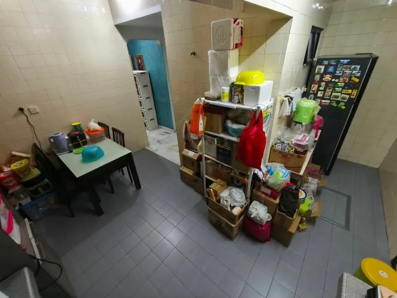Kitchen features: grey tiled flooring, white tiled walls, wooden shelving unit, black refrigerator, small dining table with black chairs, various kitchen storage containers, colorful plastic utensils, wall-mounted storage for kitchen items.