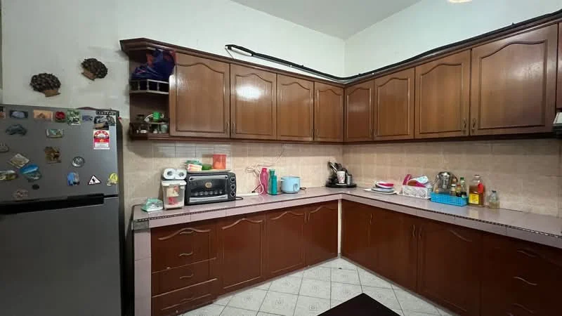 Kitchen features: brown wooden cabinetry, white tiled backsplash, grey countertop, stainless-steel fridge, built-in microwave, toaster, kettle, blue plastic storage container, various kitchen utensils, ceramic plates, floor tiles with diamond pattern, wall-mounted shelves, decorative magnets on fridge; style: traditional.